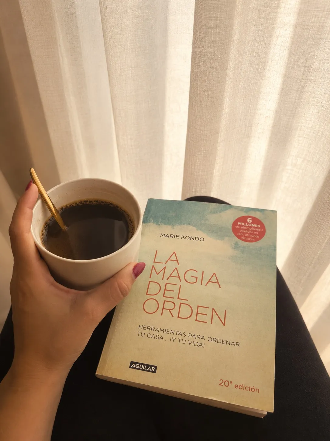 Paula holding a coffee next to Marie Kondo’s “The Life-Changing Magic of Tidying Up”, against a backlit linen curtain